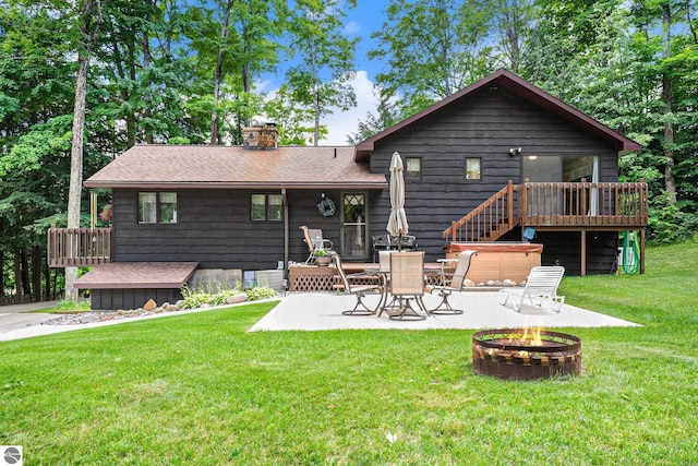 rear view of property with a lawn, a fire pit, a deck, a hot tub, and a patio