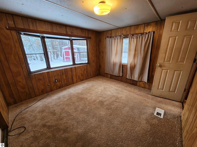 empty room with carpet flooring, a textured ceiling, and wooden walls