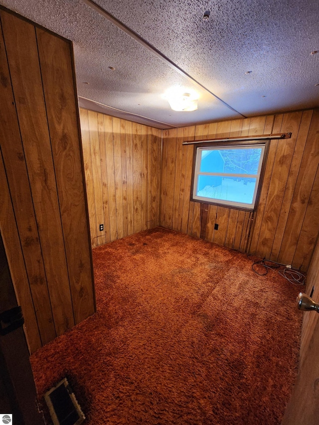 carpeted empty room with wood walls and a textured ceiling