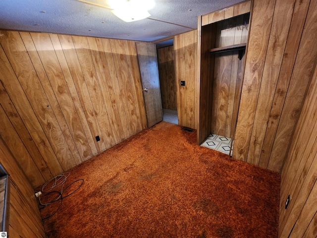 unfurnished bedroom with light carpet, a textured ceiling, a closet, and wooden walls