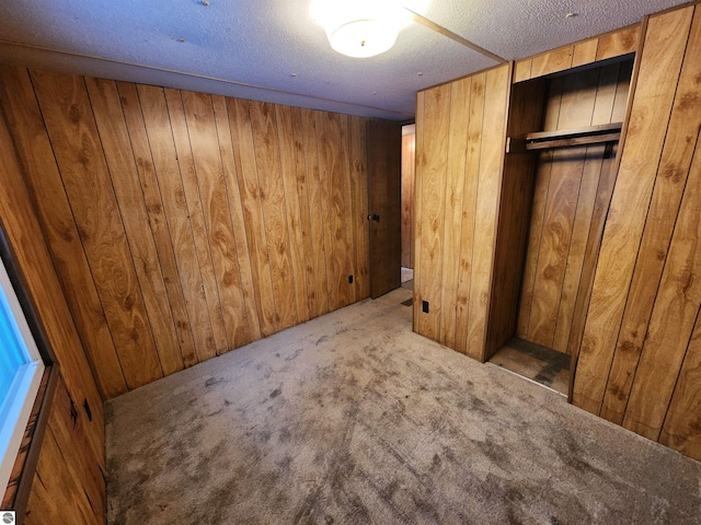 unfurnished bedroom featuring wood walls, a closet, carpet, and a textured ceiling