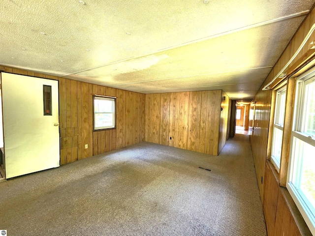 unfurnished room with wood walls, dark carpet, and a textured ceiling