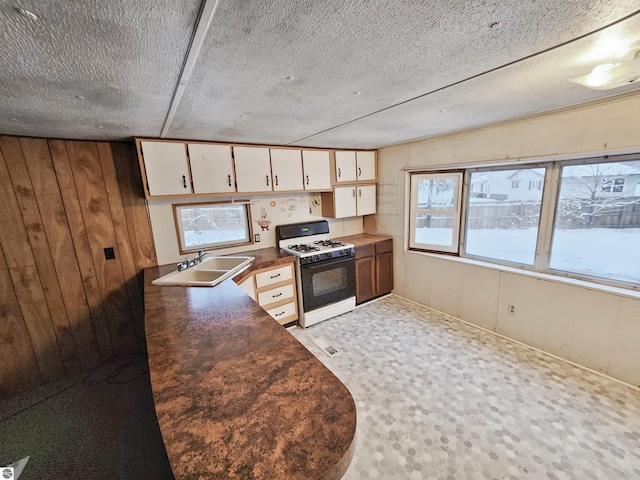 kitchen featuring white cabinets, sink, wooden walls, a textured ceiling, and white range with gas cooktop