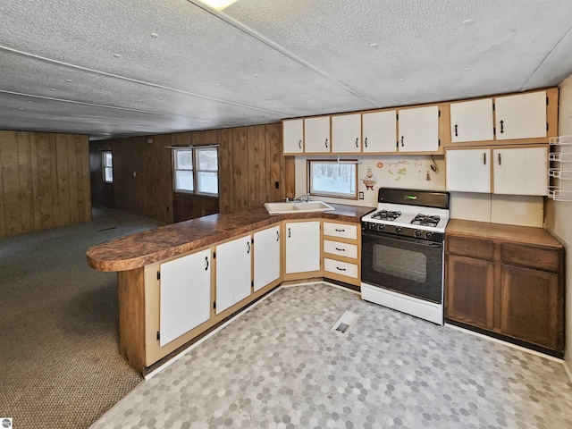 kitchen featuring wood walls, white cabinets, a textured ceiling, and white gas range oven