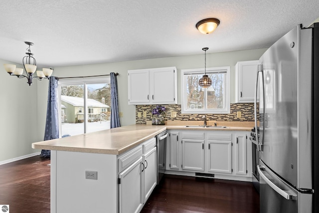 kitchen with sink, stainless steel appliances, dark wood-type flooring, kitchen peninsula, and decorative light fixtures