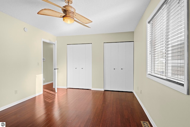 unfurnished bedroom with hardwood / wood-style floors, a textured ceiling, two closets, and ceiling fan