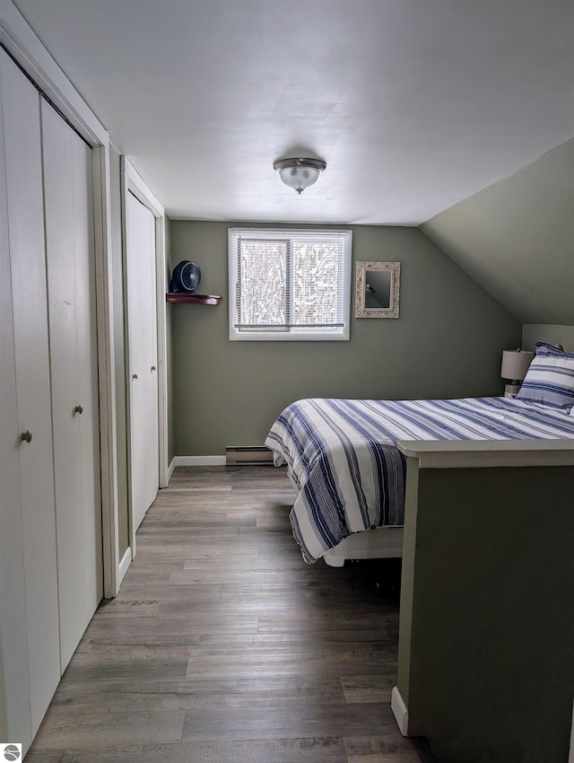 bedroom with hardwood / wood-style floors, a baseboard radiator, multiple closets, and lofted ceiling