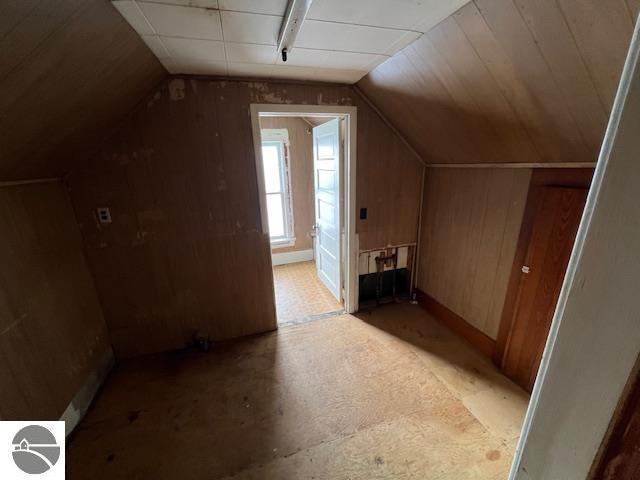 bonus room featuring vaulted ceiling and wood walls