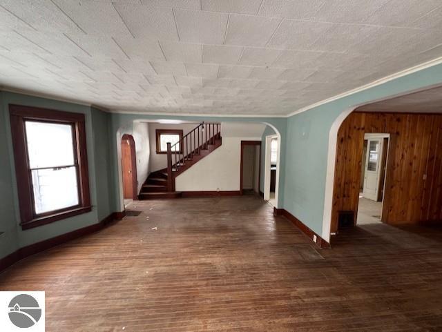 empty room with wooden walls, crown molding, and dark wood-type flooring