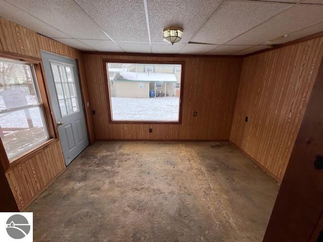 unfurnished dining area featuring a wealth of natural light, wood walls, and a drop ceiling