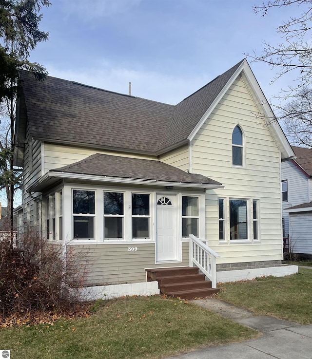 view of front of property with entry steps, a front lawn, and roof with shingles