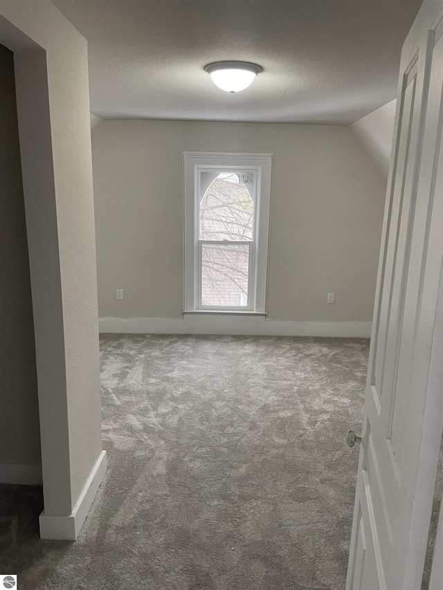 carpeted empty room with vaulted ceiling, a textured ceiling, and baseboards