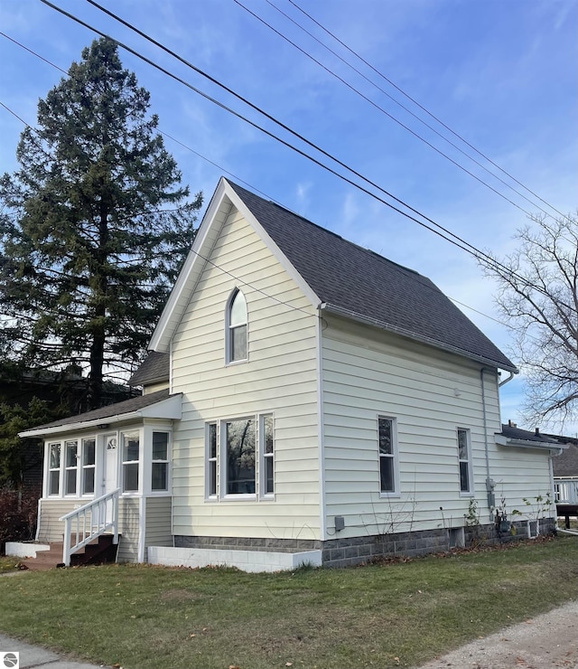 view of side of property with entry steps, roof with shingles, and a lawn