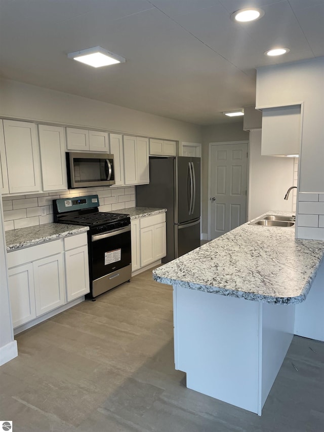 kitchen featuring stainless steel appliances, a peninsula, a sink, white cabinets, and tasteful backsplash