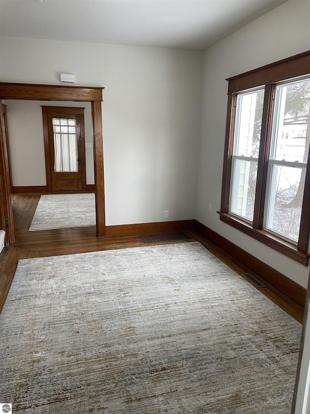 spare room featuring dark wood-style flooring, visible vents, and baseboards