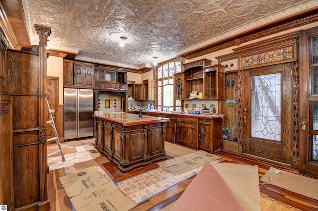 kitchen with stainless steel fridge, dark brown cabinets, a kitchen island with sink, and ornamental molding