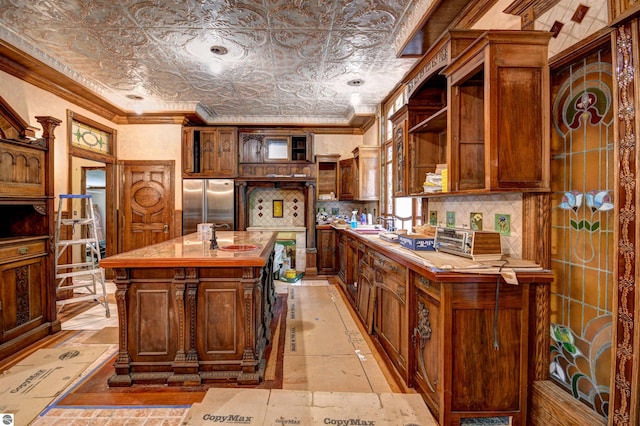 kitchen with a center island with sink, sink, stainless steel fridge, ornamental molding, and tasteful backsplash