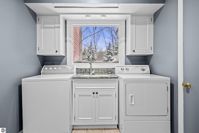 clothes washing area with cabinets, washing machine and dryer, light tile patterned flooring, and sink