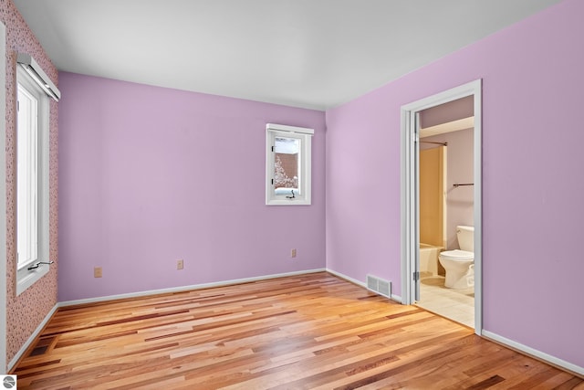 unfurnished bedroom with ensuite bathroom, light wood-type flooring, and multiple windows