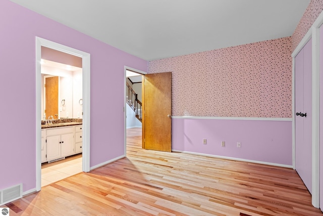 unfurnished bedroom with ensuite bathroom, light hardwood / wood-style flooring, and sink