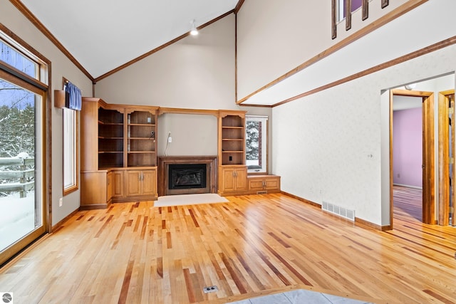 unfurnished living room with light wood-type flooring, high vaulted ceiling, and crown molding