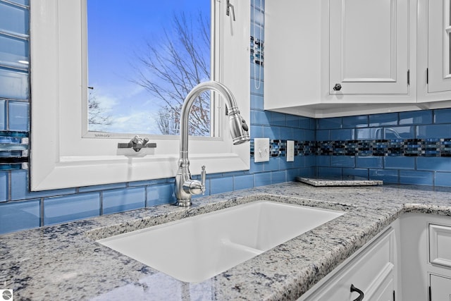 details featuring white cabinets, backsplash, light stone countertops, and sink