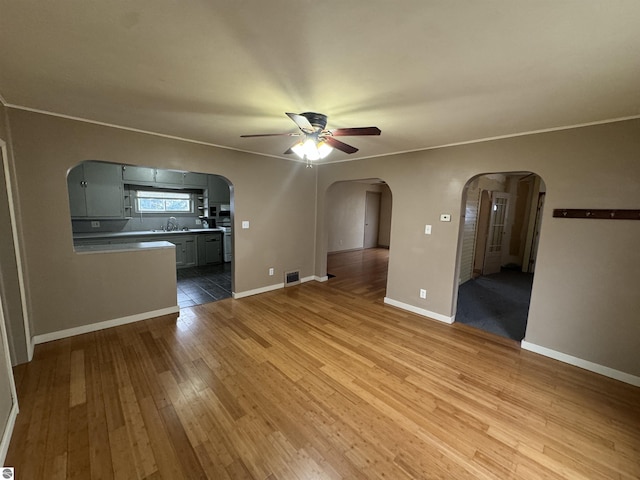 unfurnished living room featuring ceiling fan, sink, ornamental molding, and light wood-type flooring