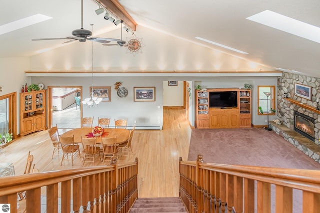 living room featuring light wood-type flooring, track lighting, vaulted ceiling with skylight, ceiling fan with notable chandelier, and a fireplace