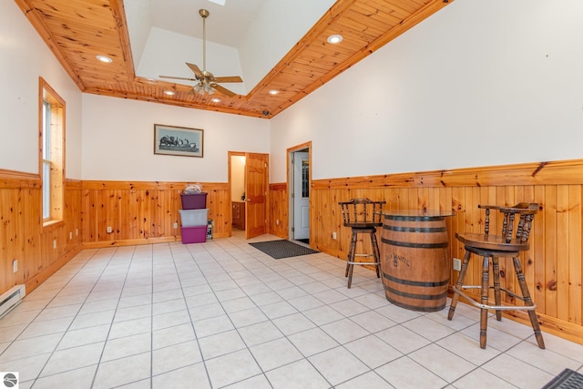 living area with ceiling fan, lofted ceiling with skylight, wooden walls, light tile patterned floors, and ornamental molding