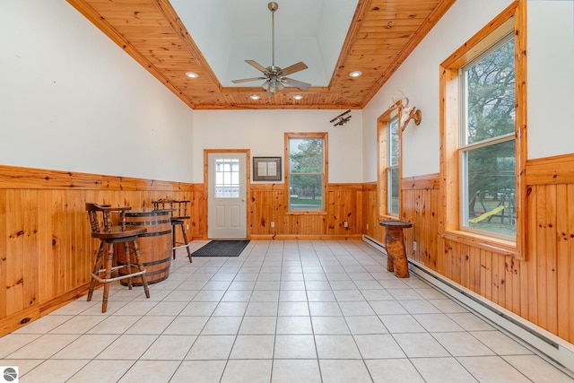 tiled foyer entrance with ceiling fan, wood walls, baseboard heating, and crown molding