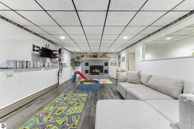 living room featuring a paneled ceiling, wood-type flooring, and a brick fireplace