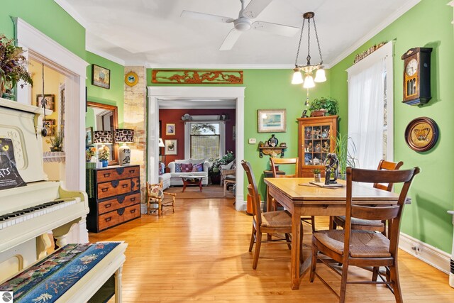 dining area featuring a ceiling fan, baseboards, crown molding, and light wood-style flooring