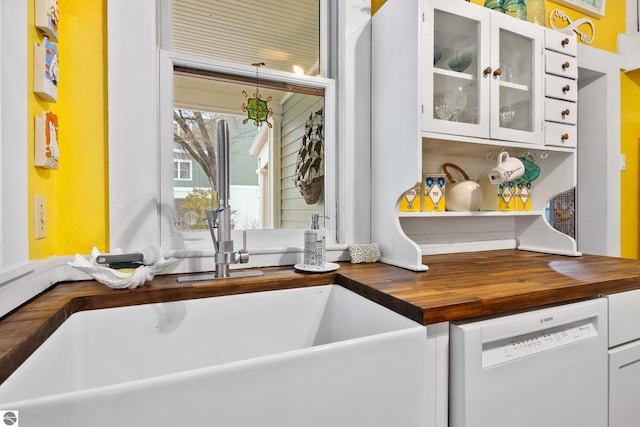 interior details with wood counters, dishwasher, white cabinets, and glass insert cabinets