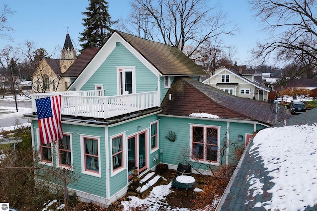 snow covered house featuring entry steps and a balcony