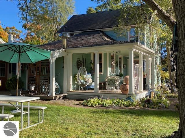 back of property featuring a yard, roof with shingles, and a porch