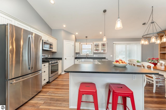 kitchen with hanging light fixtures, a kitchen breakfast bar, light hardwood / wood-style flooring, white cabinets, and appliances with stainless steel finishes