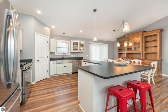 kitchen with white cabinetry, lofted ceiling, a kitchen bar, appliances with stainless steel finishes, and hardwood / wood-style flooring