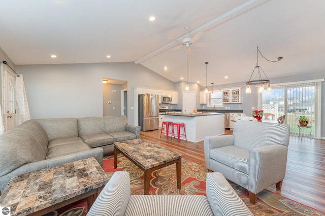 living room featuring vaulted ceiling with beams, light wood-type flooring, and ceiling fan with notable chandelier