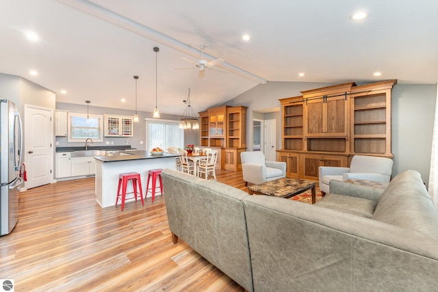 living room with ceiling fan, sink, light hardwood / wood-style floors, and vaulted ceiling