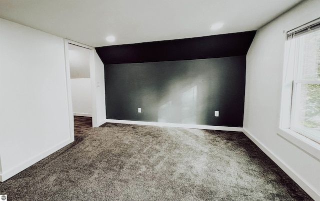 spare room featuring lofted ceiling and dark colored carpet