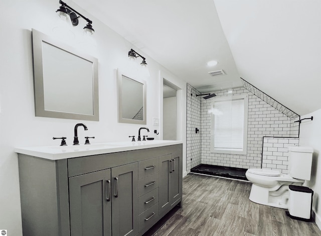 bathroom with hardwood / wood-style floors, vanity, lofted ceiling, toilet, and a tile shower