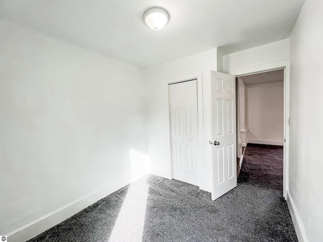 unfurnished bedroom with dark colored carpet and a closet