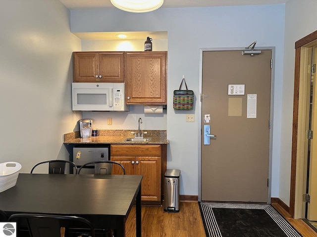 kitchen with dark hardwood / wood-style flooring, light stone counters, sink, and stainless steel dishwasher