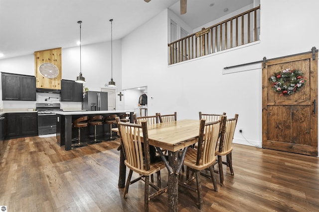 dining room with a barn door, dark hardwood / wood-style flooring, and high vaulted ceiling