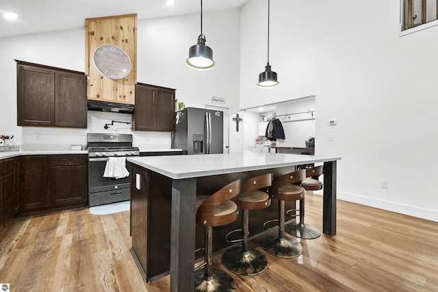 kitchen featuring a center island, high vaulted ceiling, a breakfast bar area, light wood-type flooring, and stainless steel appliances