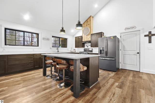 kitchen with a kitchen bar, appliances with stainless steel finishes, dark brown cabinetry, high vaulted ceiling, and a kitchen island