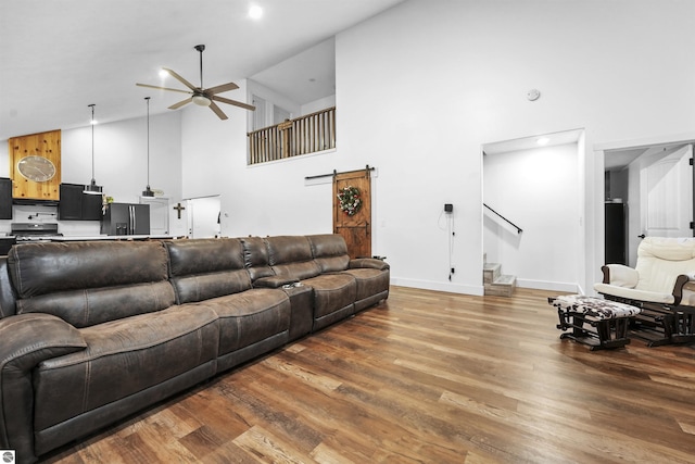 living room featuring hardwood / wood-style floors, ceiling fan, a barn door, and high vaulted ceiling