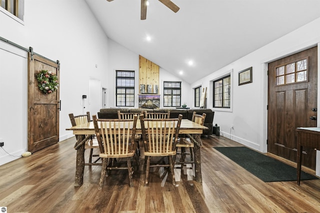 dining space with a barn door, ceiling fan, high vaulted ceiling, and wood-type flooring