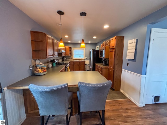 kitchen with a breakfast bar, hanging light fixtures, dark hardwood / wood-style flooring, kitchen peninsula, and stainless steel appliances