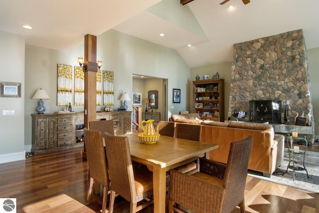 dining space featuring hardwood / wood-style floors, ceiling fan, a stone fireplace, and vaulted ceiling